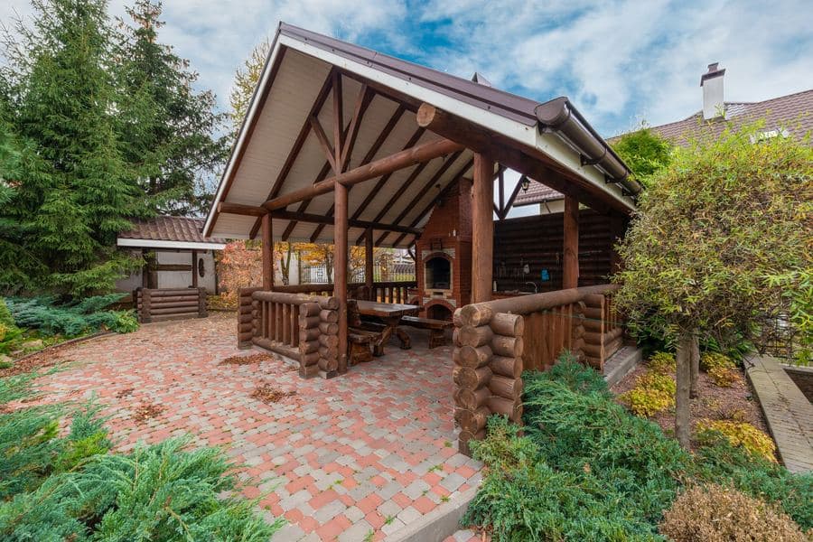 Timber shade structure with heavy posts and open rafters standing in a planted garden