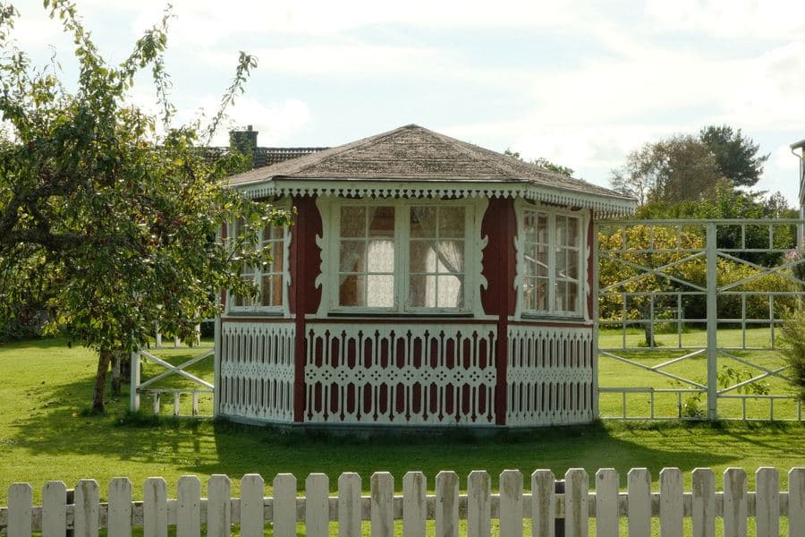 Octagonal garden gazebo standing on a lawn in a planted backyard in daylight