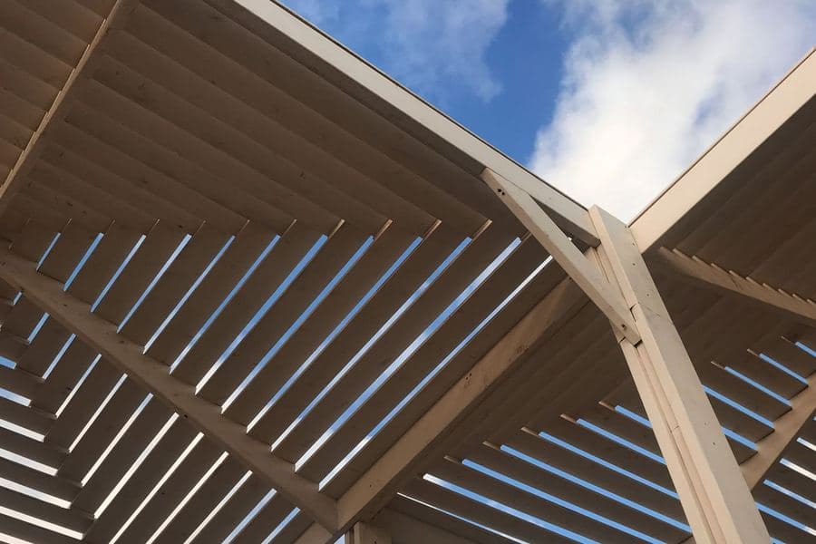 Timber pergola beams seen from below against a bright sky with passing cloud