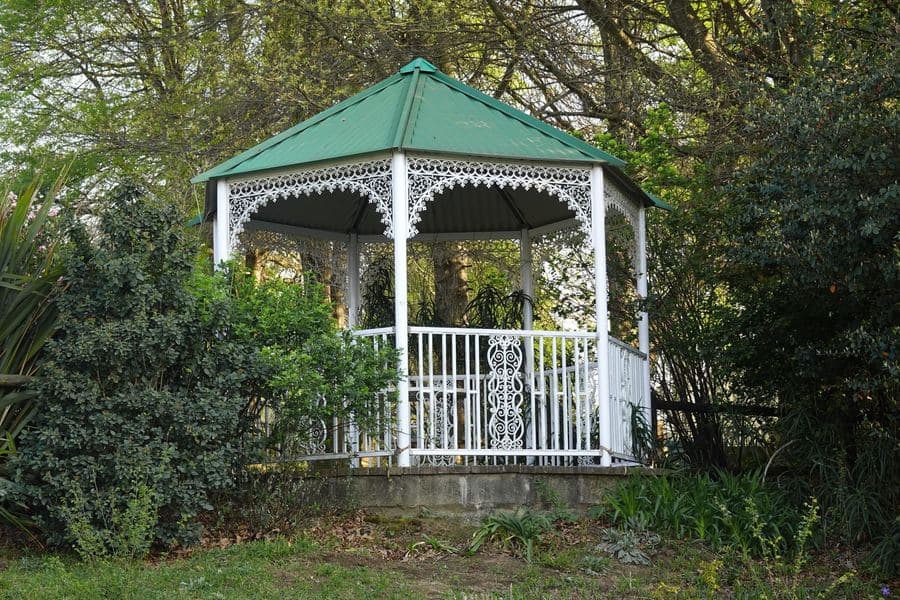 White garden gazebo surrounded by dense green planting, roof and posts visible in daylight