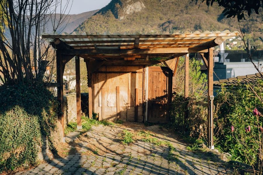 Site-built timber shelter with rough-sawn posts and an open rafter roof over a stone yard