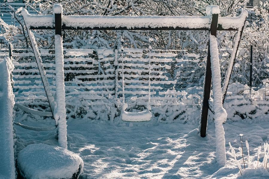 Snow lying on a garden structure and surrounding shrubs under a grey winter sky