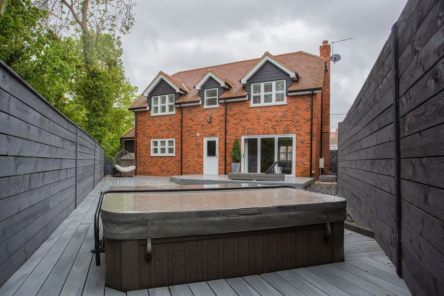 Covered hot tub on a gray composite deck in an enclosed backyard with no overhead shade