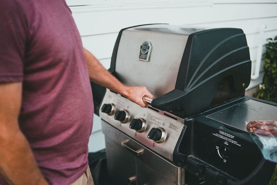 Person operating the controls on a stainless gas grill on a patio beside a house wall