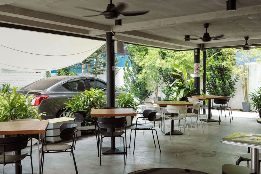 Outdoor cafe terrace with tables and chairs shaded by planting and overhead cover