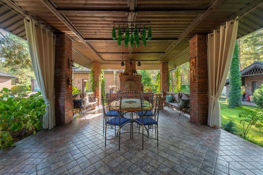 Solid-roofed backyard pavilion with brick piers and timber beams over a paved dining area