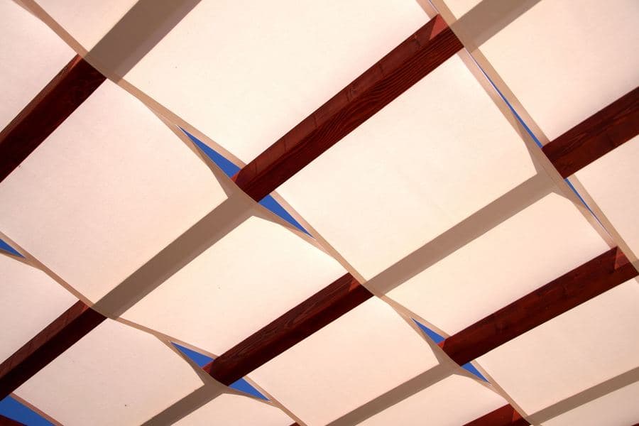 Fabric shade cover fitted over pergola rafters above an outdoor dining area
