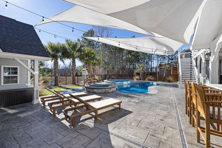 Overlapping white shade sails tensioned above loungers beside a backyard swimming pool
