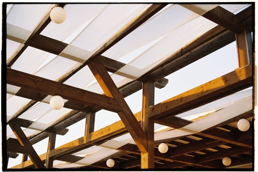 Timber pergola with white fabric shade panels and hanging bulb lights above a terrace