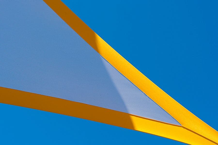 Close-up of a tensioned shade sail fabric showing its knitted mesh weave against the sky