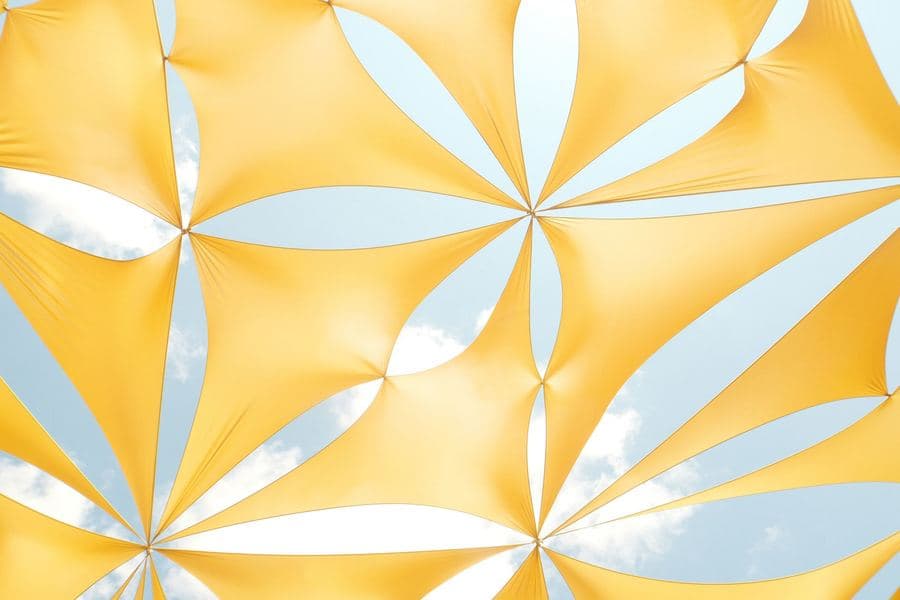 Overlapping tensioned shade sails seen from below against a bright sky