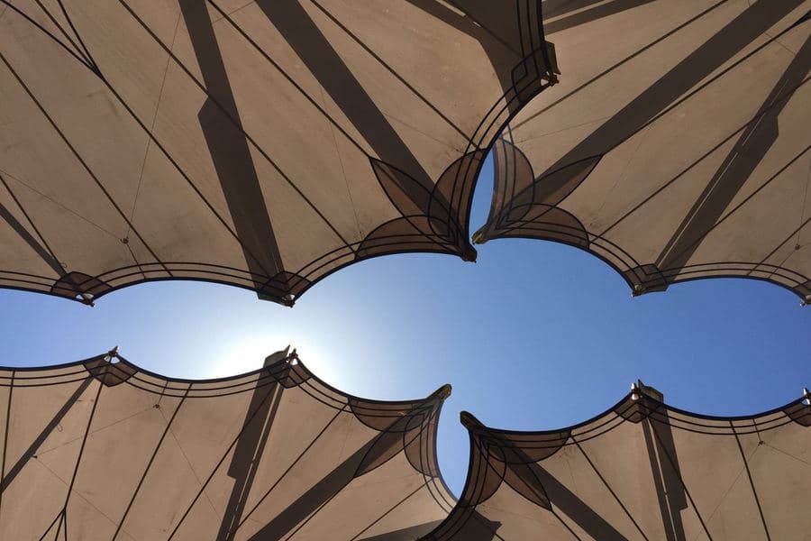 Low-angle view of geometric fabric canopies against a bright blue sky