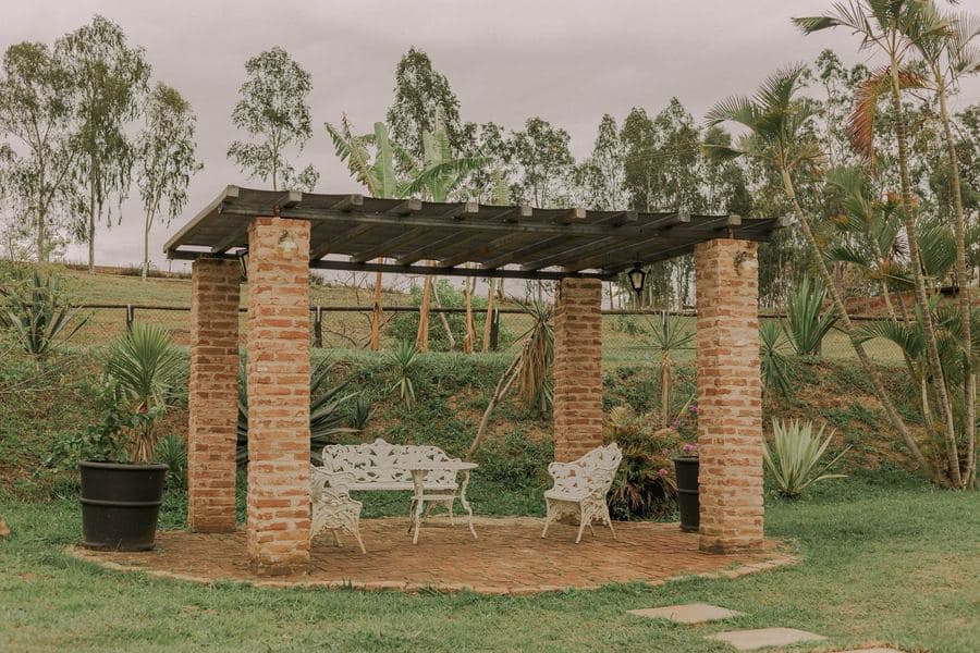 Rustic pergola with white outdoor furniture surrounded by green planting