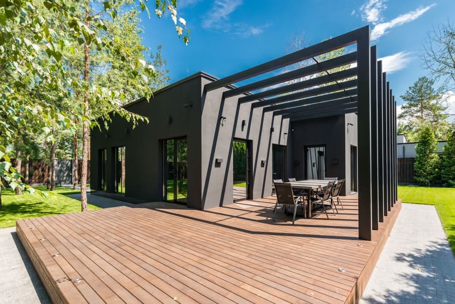 Wood-grain finish aluminum louvered pergola attached to a house wall above outdoor seating