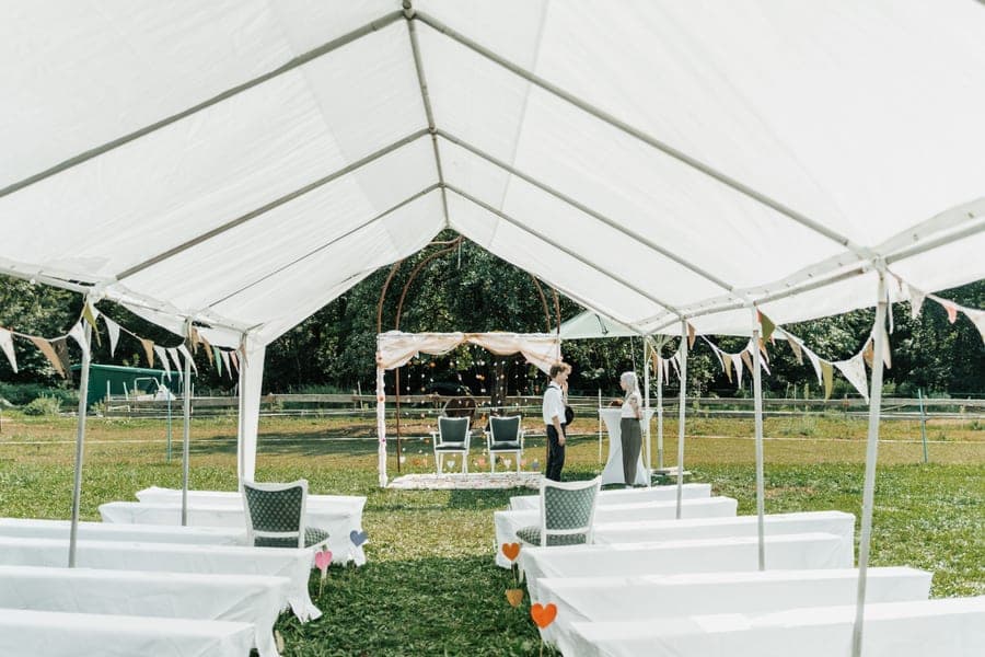 White aluminum-framed pop-up canopy set up on grass with sidewalls partly attached
