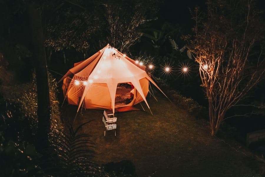 Six-sided portable screen gazebo lit from inside on a lawn at dusk
