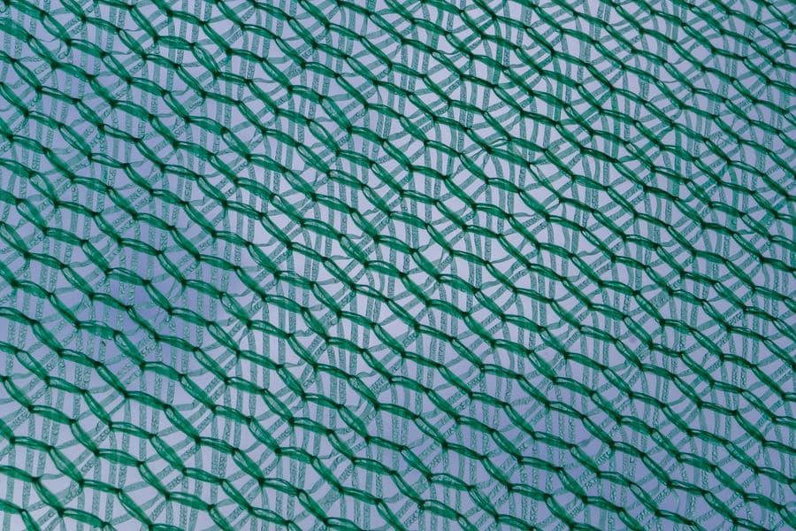 Roll of knitted shade fabric mesh showing the open weave against the sky
