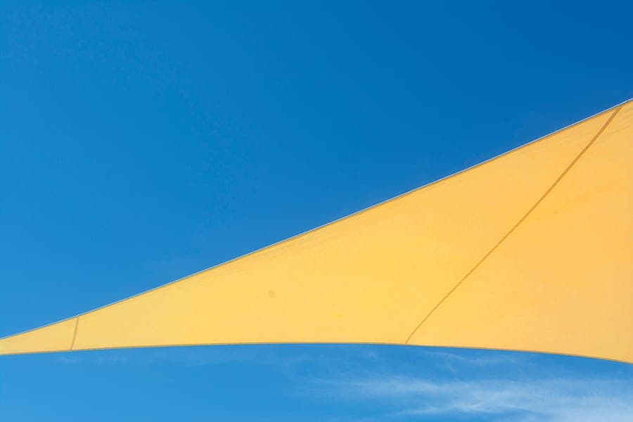 Triangular beige shade sail tensioned between three anchor points over a garden deck